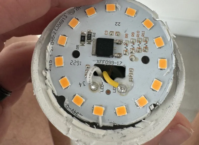 Opened LED bulb showing a circular circuit board ringed with small orange phosphor-coated LED chips