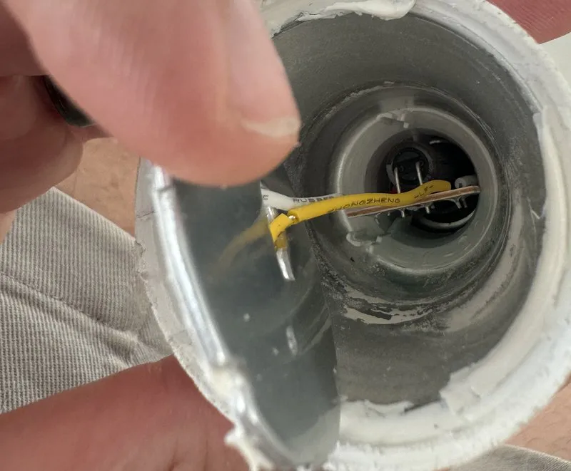 Hand holding a disassembled LED bulb, with wires running into its hollow base